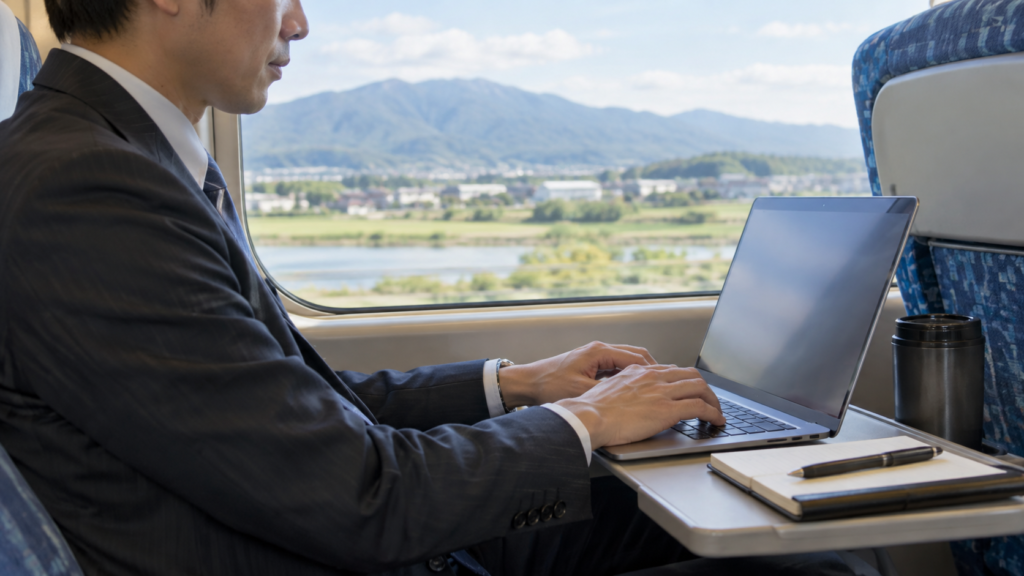 出張の移動中に列車内でパソコン業務をする会社員